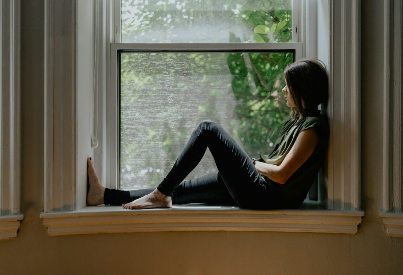 Femme pensive assise sur le rebord d'une fenêtre