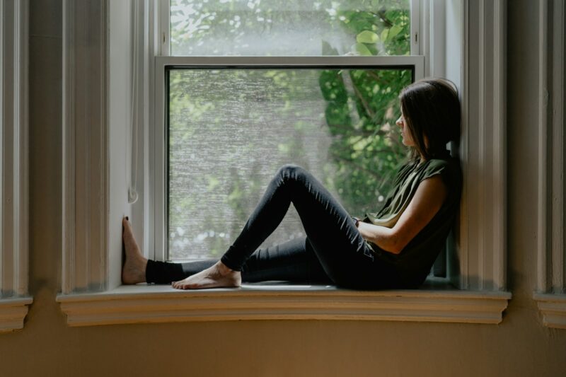 Femme pensive assise sur le rebord d'une fenêtre